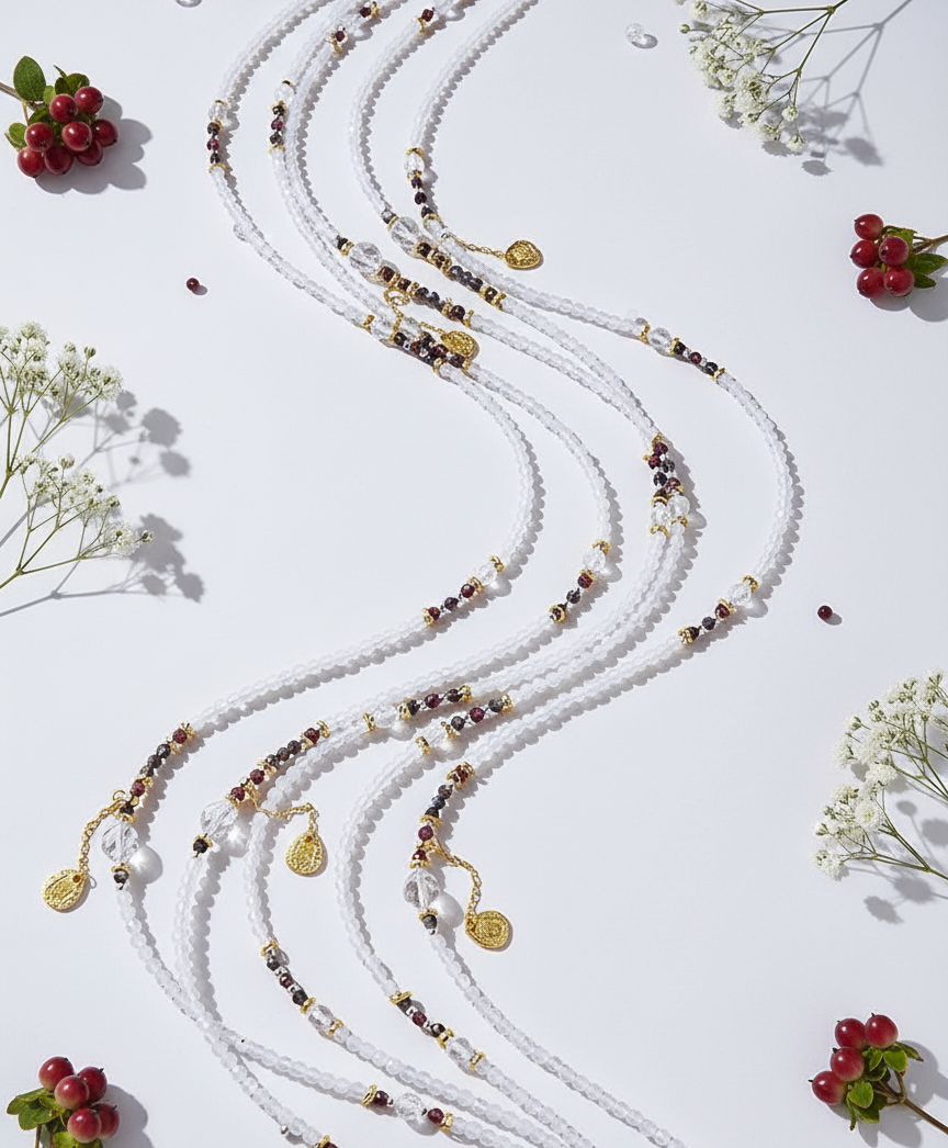 White beaded necklace with gold accents on a white background with small red flowers and green leaves.