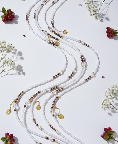 White beaded necklace with gold accents on a white background with small red flowers and green leaves.
