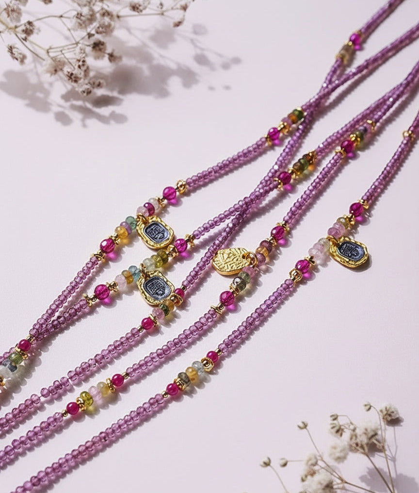Pink beaded necklaces with gold and blue accents on a light pink background with dried flowers.