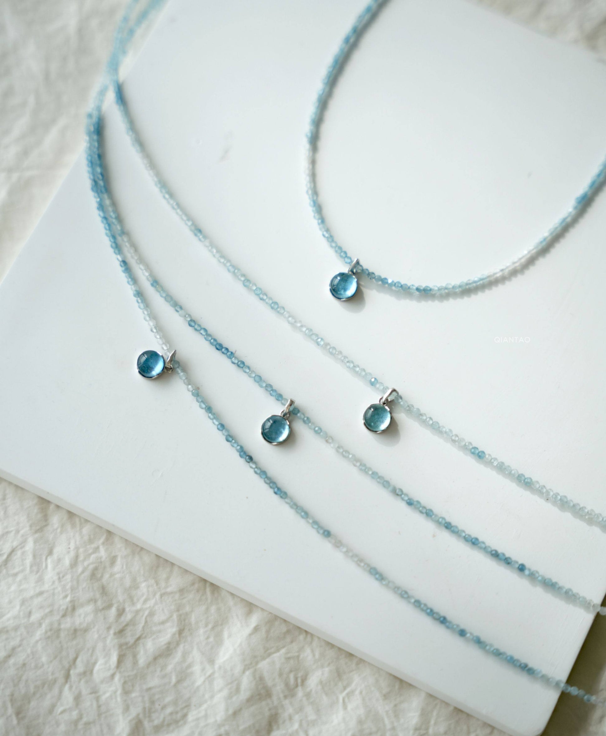 Three blue beaded necklaces on a white surface