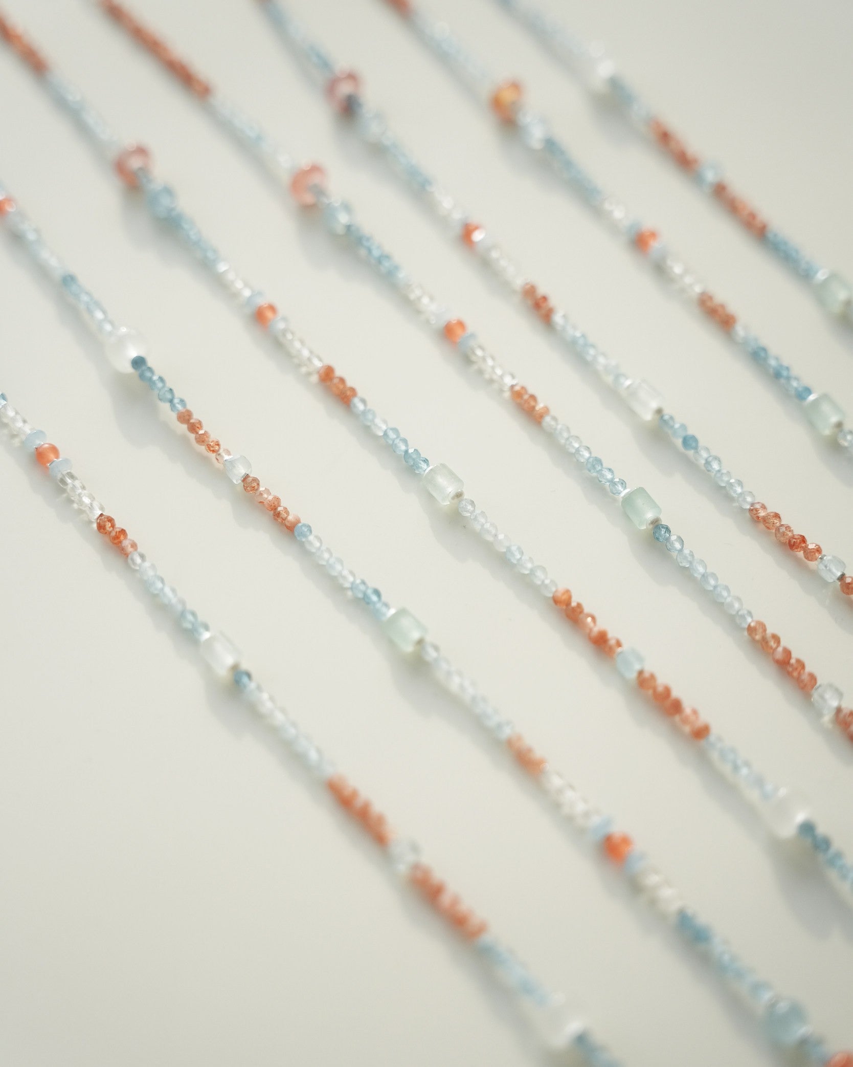 Close-up of beaded necklaces with orange, blue, and white beads on a light background
