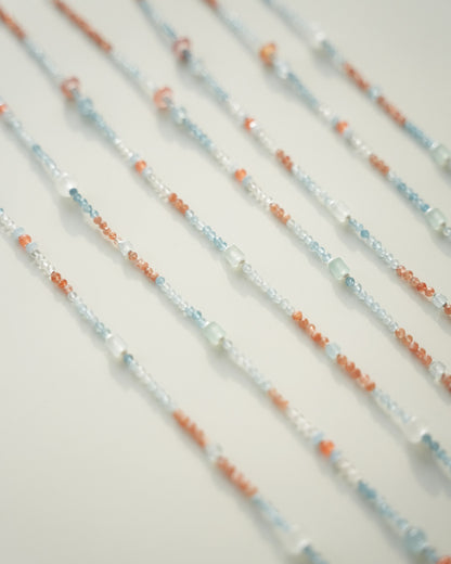 Close-up of beaded necklaces with orange, blue, and white beads on a light background