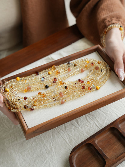 Beaded necklace on a wooden tray held by a person wearing a brown sweater.