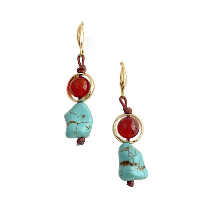 Pair of earrings with turquoise stones and red beads on a white background