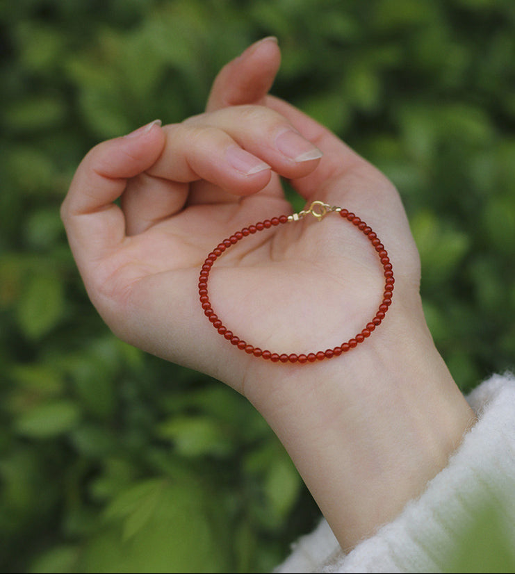 Hand holding a red beaded bracelet against a green background