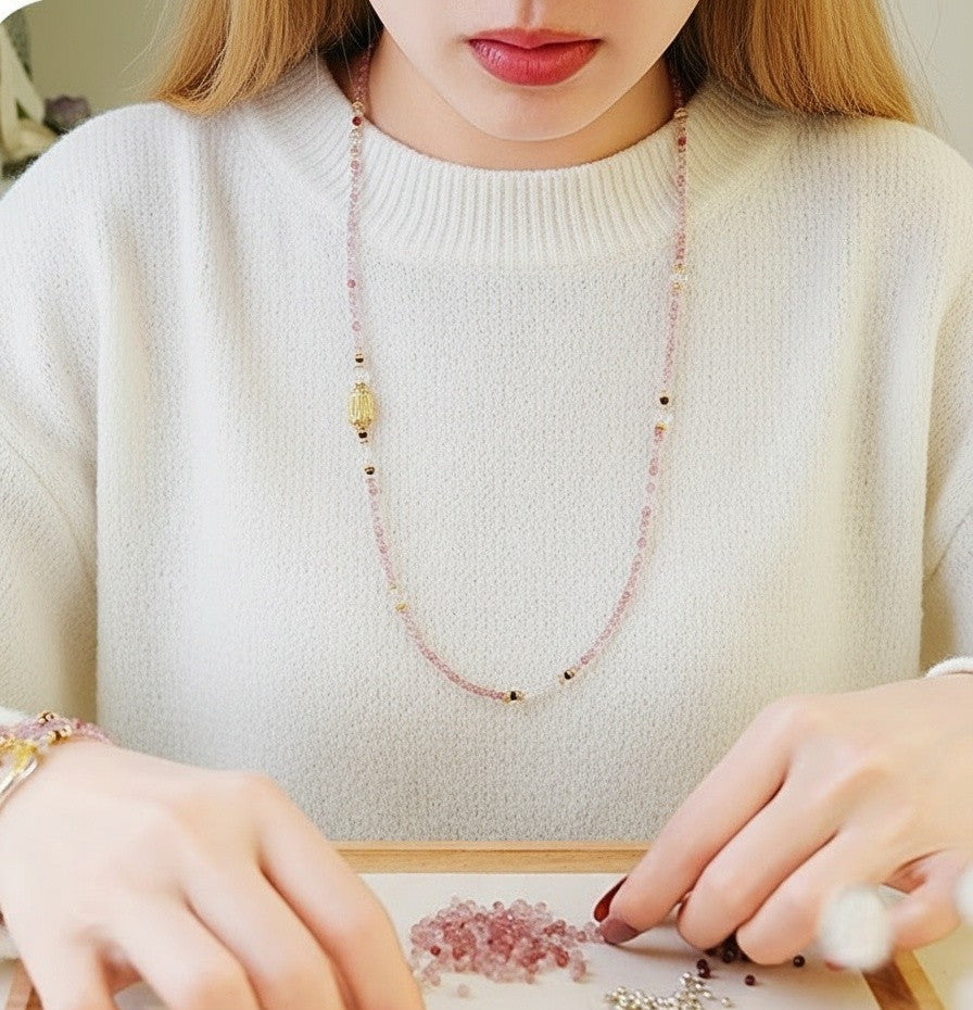 Person wearing a beaded necklace and white sweater, sitting at a table with a small object.