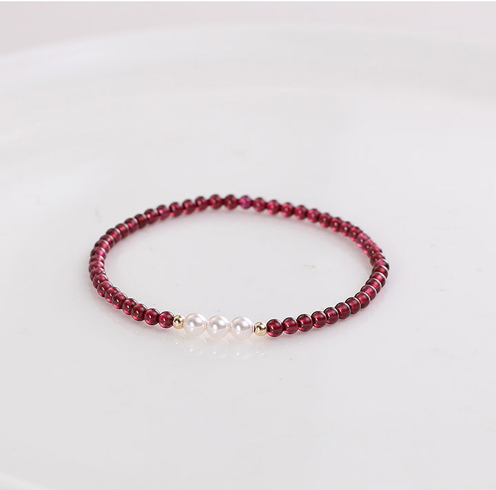 A bracelet with deep red natural garnet beads and white freshwater pearls, with gold-toned spacers and a comfortable elastic fit.