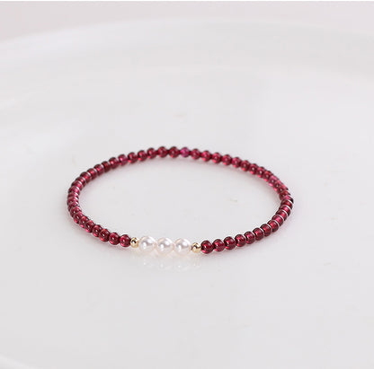 A bracelet with deep red natural garnet beads and white freshwater pearls, with gold-toned spacers and a comfortable elastic fit.