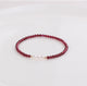 A bracelet with deep red natural garnet beads and white freshwater pearls, with gold-toned spacers and a comfortable elastic fit.
