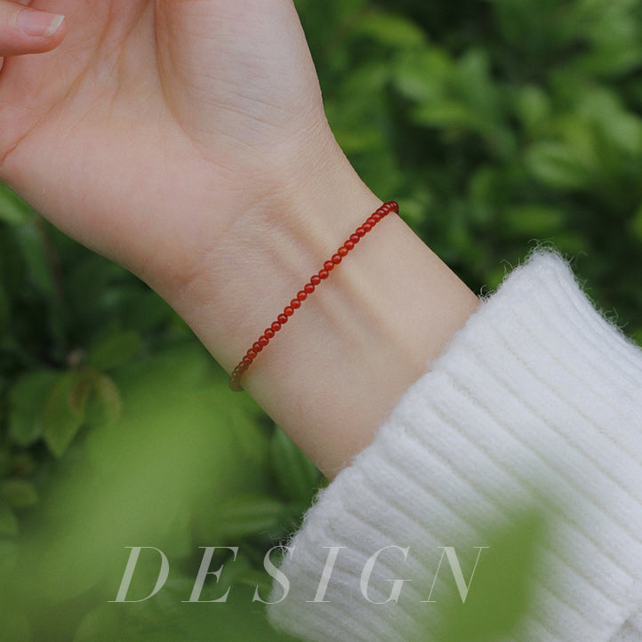 Hand wearing a red beaded bracelet with a green blurred background