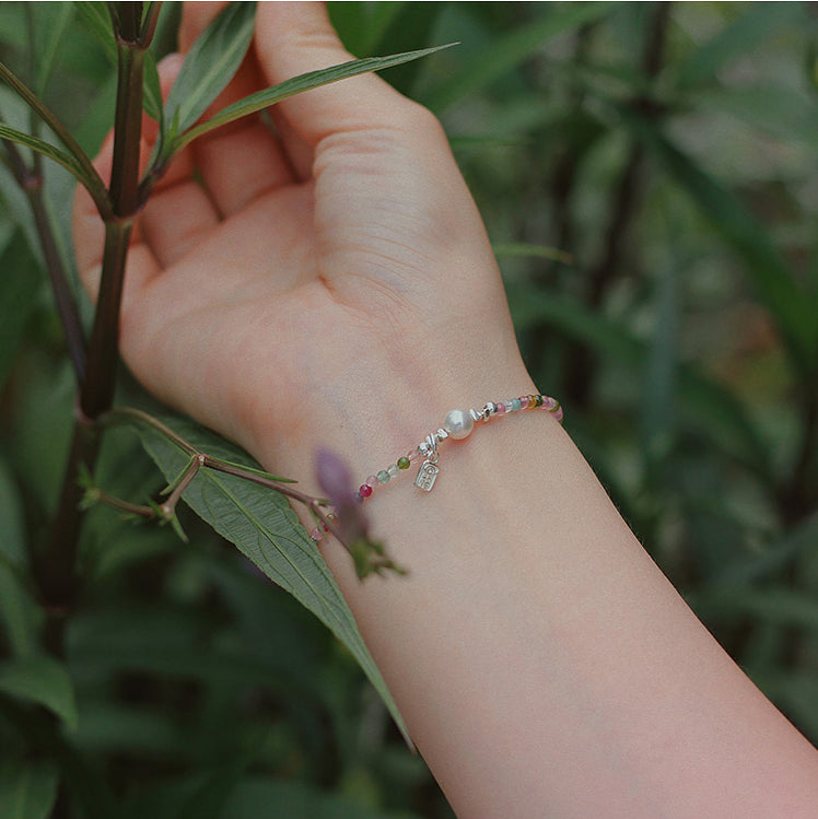 Hand wearing a bracelet with greenery in the background