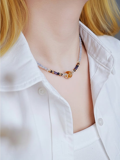 Necklace with multicolored beads worn by a person in a white shirt.