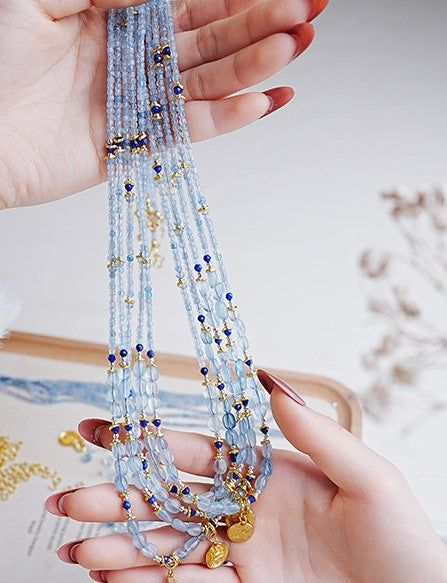 Hand holding a multi-strand beaded necklace with blue and gold beads against a blurred background.