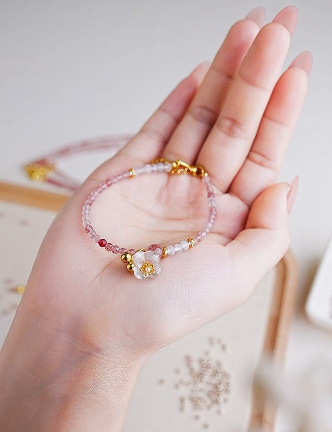 Hand wearing a beaded bracelet with floral charm on a light background