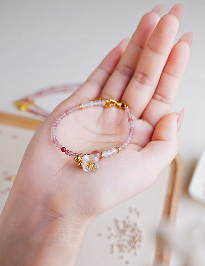 Hand wearing a beaded bracelet with floral charm on a light background