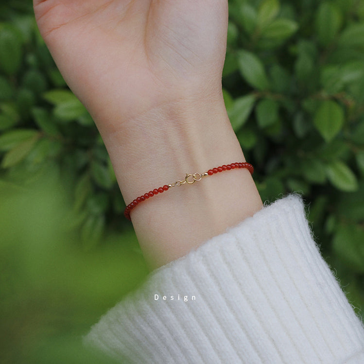 Red beaded bracelet on a wrist with a green leafy background