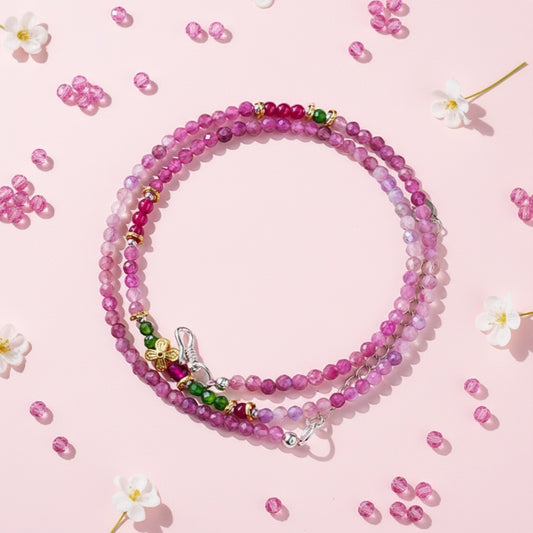 Stack of pink beaded necklaces on a pink background with scattered beads and flowers.