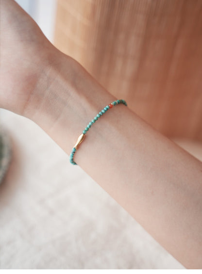 Close-up of a wrist wearing a turquoise beaded bracelet with a gold accent on a blurred background.