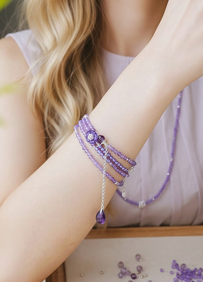 Close-up of a person's arm wearing multiple purple beaded bracelets with a blurred background.