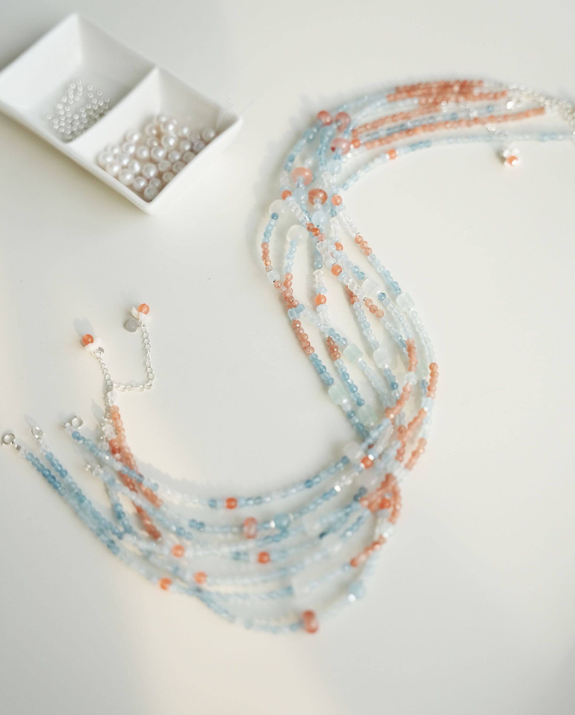 Beaded necklaces with small containers of beads on a light background