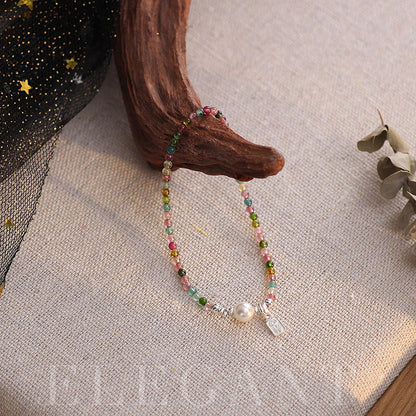 Multicolored beaded bracelet with a pearl charm on a textured surface.