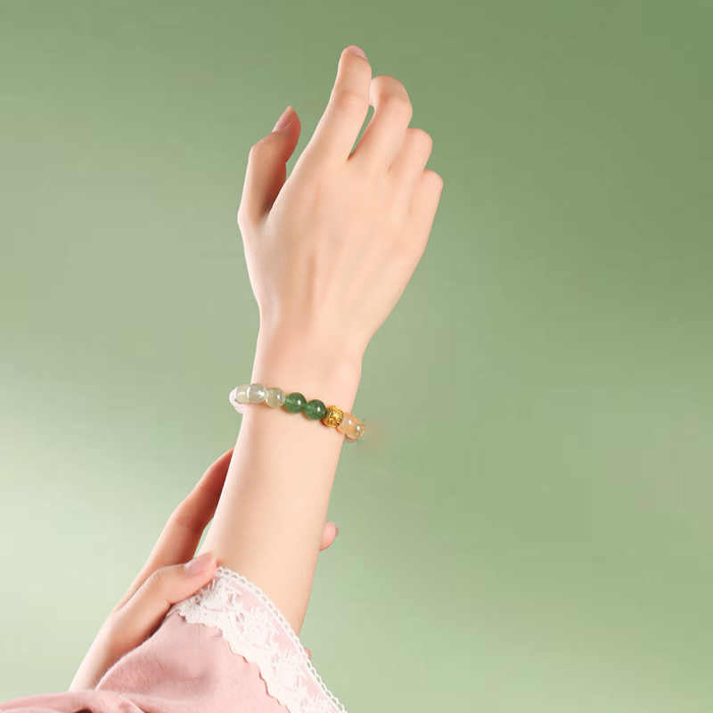 Hand wearing a bracelet with green beads against a light green background