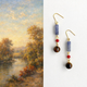 Pair of earrings with beads against a landscape painting background