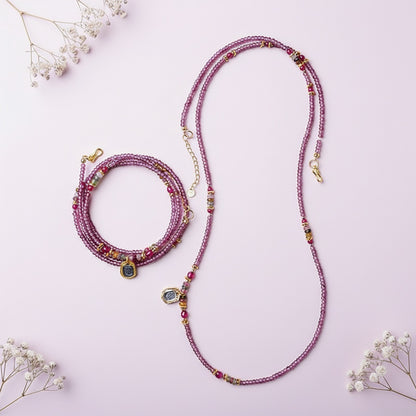 Multicolored beaded necklace and bracelet on a pink background with small white flowers.