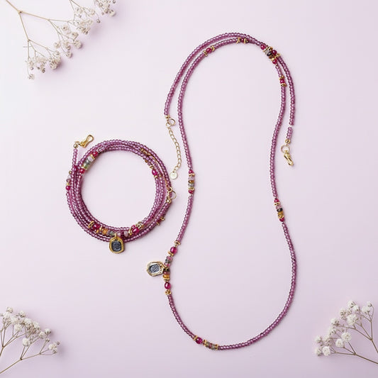 Multicolored beaded necklace and bracelet on a pink background with small white flowers.