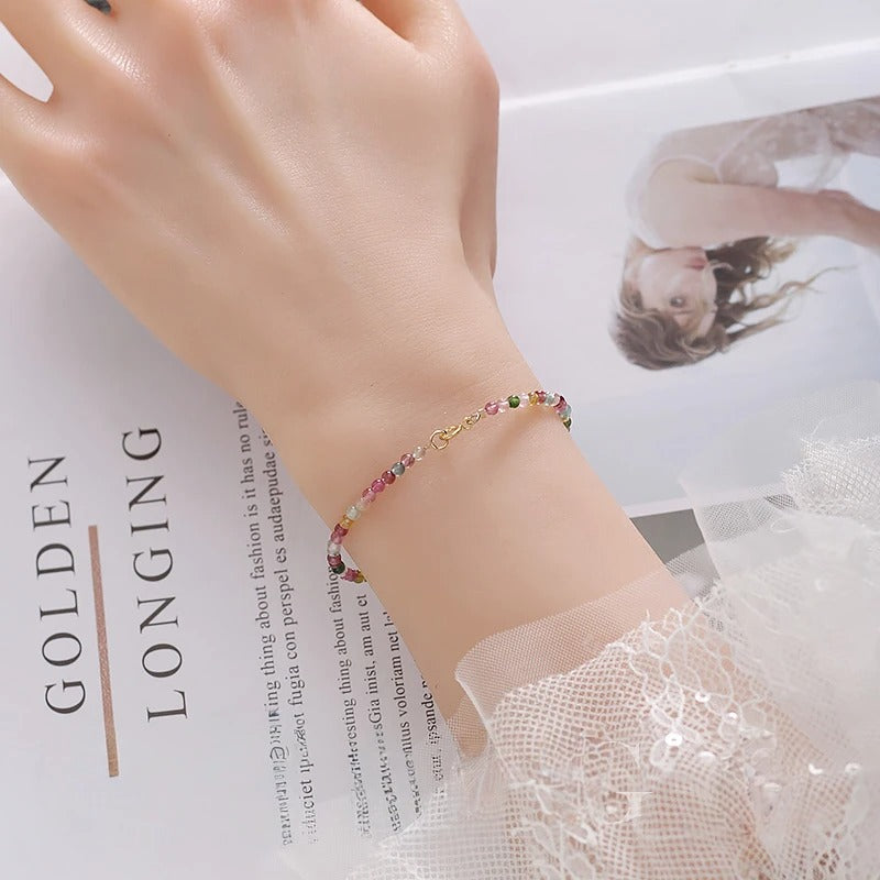 Close-up of a hand wearing a colorful beaded bracelet on a magazine background.