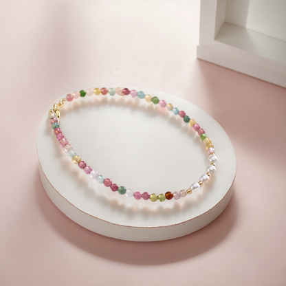 Multicolored beaded necklace on a round white stand with a soft pink background.