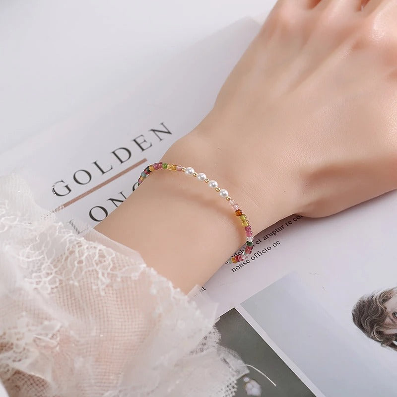 Woman's wrist wearing a colorful beaded bracelet with a book in the background.