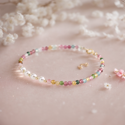 A multicolor tourmaline and freshwater pearl bracelet with gold-plated accents, displayed on a pink background with white flowers.