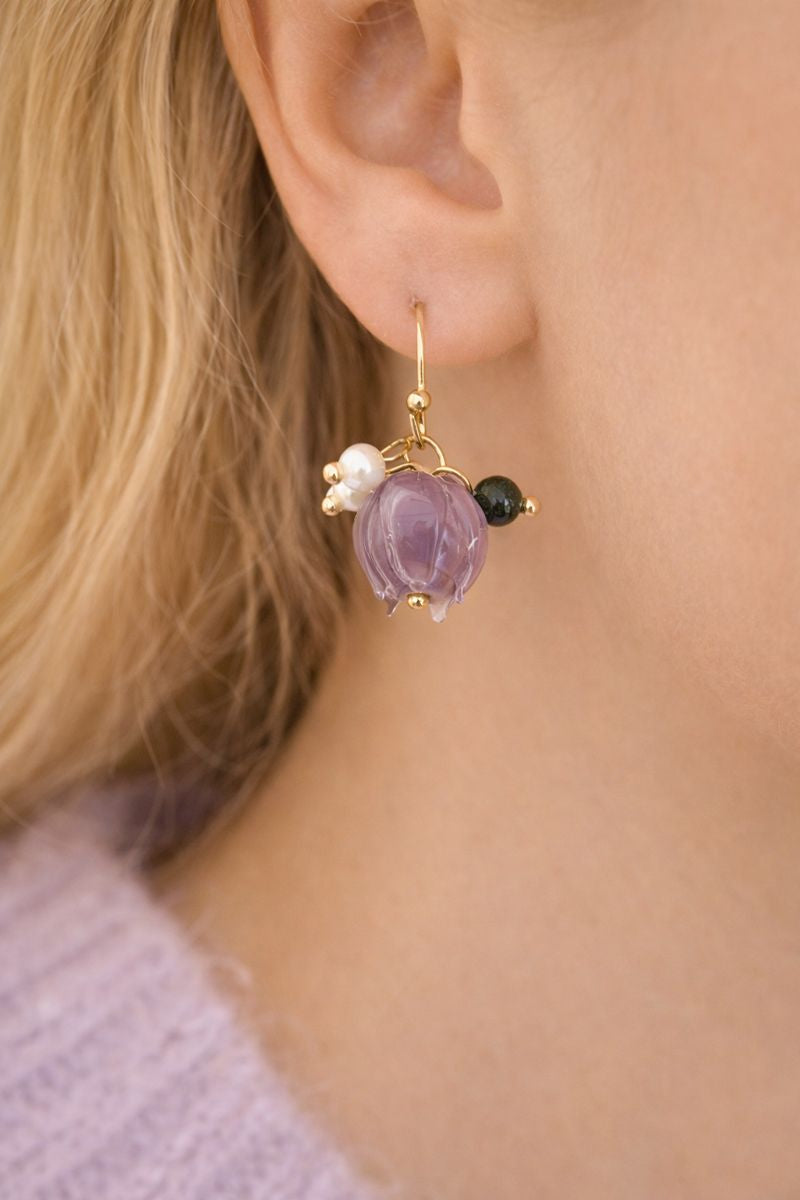 Close-up of an ear wearing a gold earring with purple gemstone, pearl, and black stone.