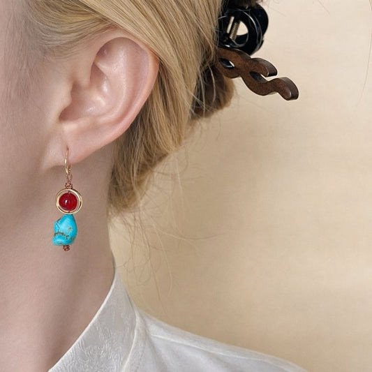 Close-up of an ear wearing a turquoise and red earring against a beige background