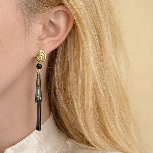Close-up of a person wearing a gold and black earring with blonde hair.