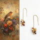 Pair of gold earrings with gemstones next to a floral painting with a bird and butterfly.