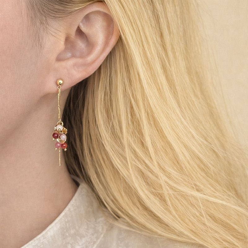 Close-up of a person wearing a gold earring with pink beads.