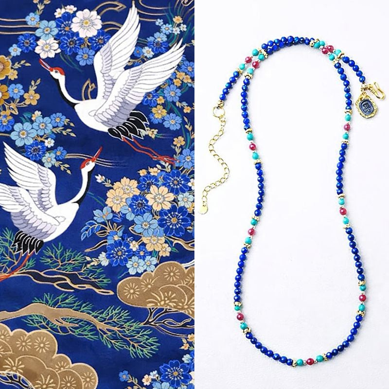Beaded necklace with blue, red, and green beads on a white background, next to a decorative fabric with cranes and flowers.