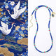 Beaded necklace with blue, red, and green beads on a white background, next to a decorative fabric with cranes and flowers.