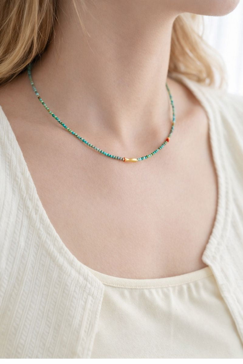 Necklace with small beads worn by a person in a white top