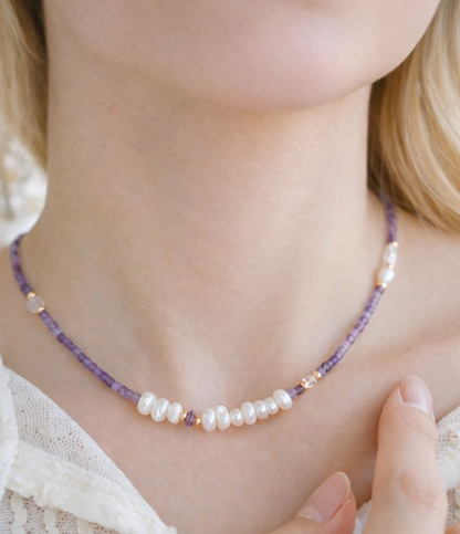 Close-up of a necklace with purple and white beads on a person wearing a lace top.