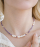 Close-up of a necklace with purple and white beads on a person wearing a lace top.