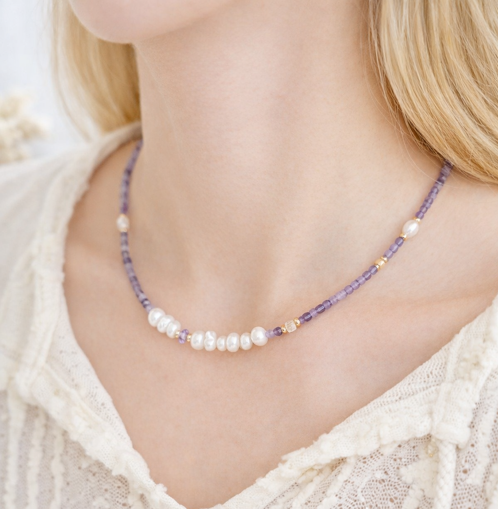 Necklace with purple beads and pearls worn by a person in a white lace top.