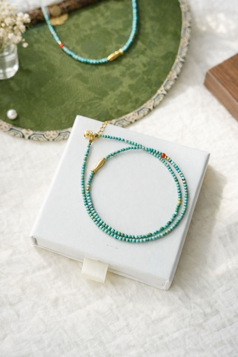 Turquoise beaded necklace on a white box with a green textured surface in the background