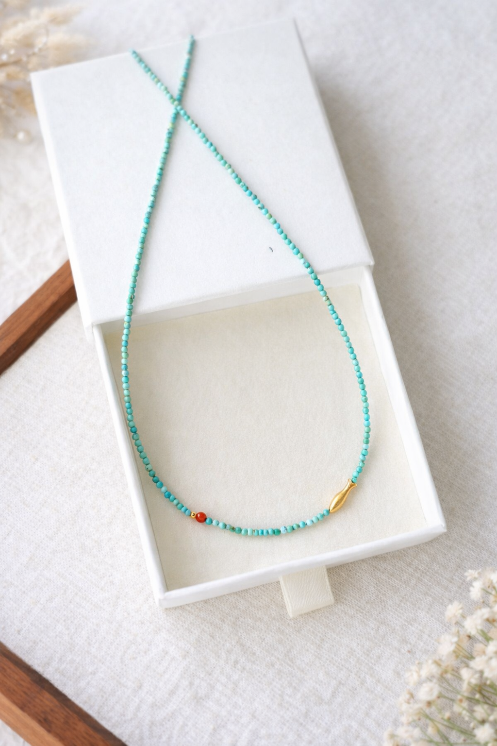 Turquoise beaded necklace with a red bead in a white jewelry box on a light background