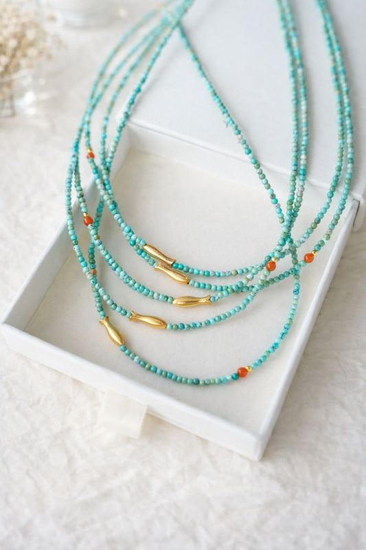 Turquoise beaded necklaces with gold accents on a white box