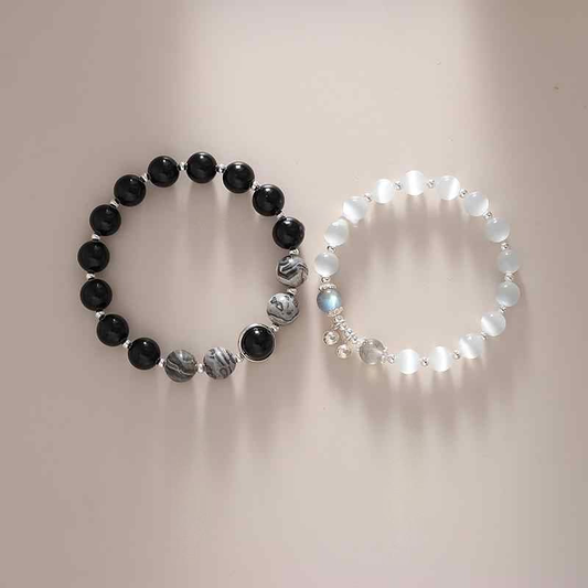 A set of two bracelets, one with black onyx beads and silver accents, and the other with moonstone beads and silver accents, displayed against a neutral background.