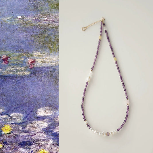 Beaded necklace with purple and white beads on a light gray background, next to a painting of water lilies.