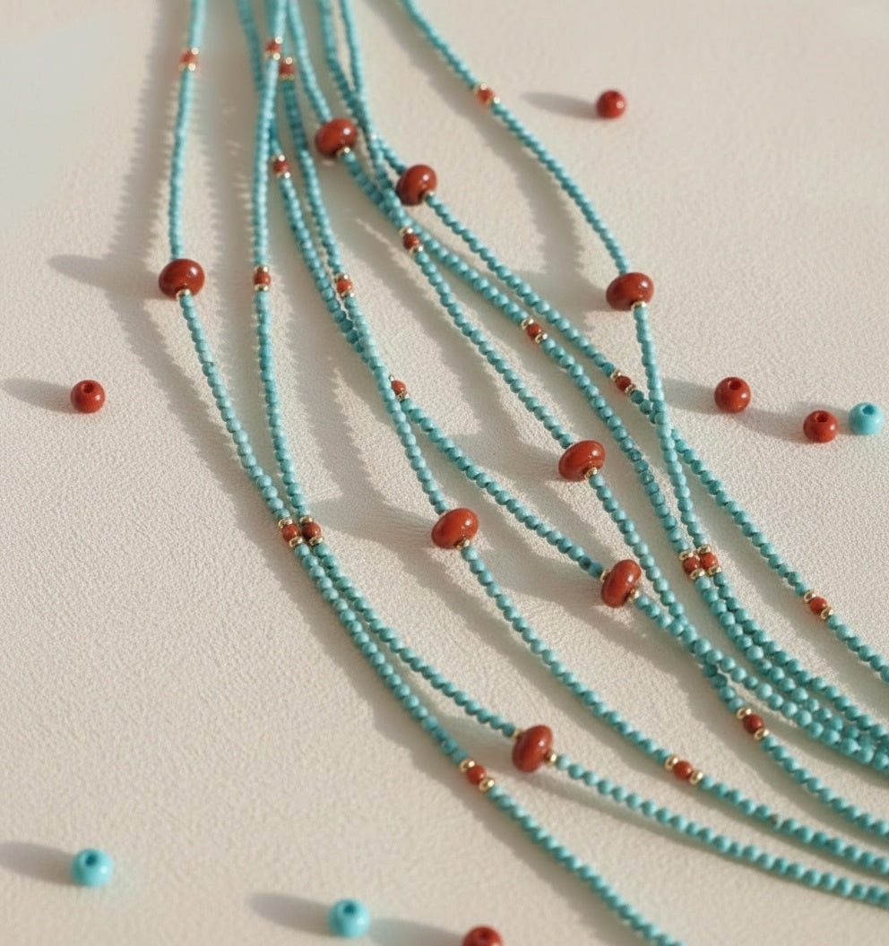 Turquoise beaded necklace with red beads on a light beige background